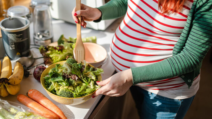 Abbildung einer schwangeren Frau welche sich mit unterschiedlichen Zutaten einen Salat zubereitet