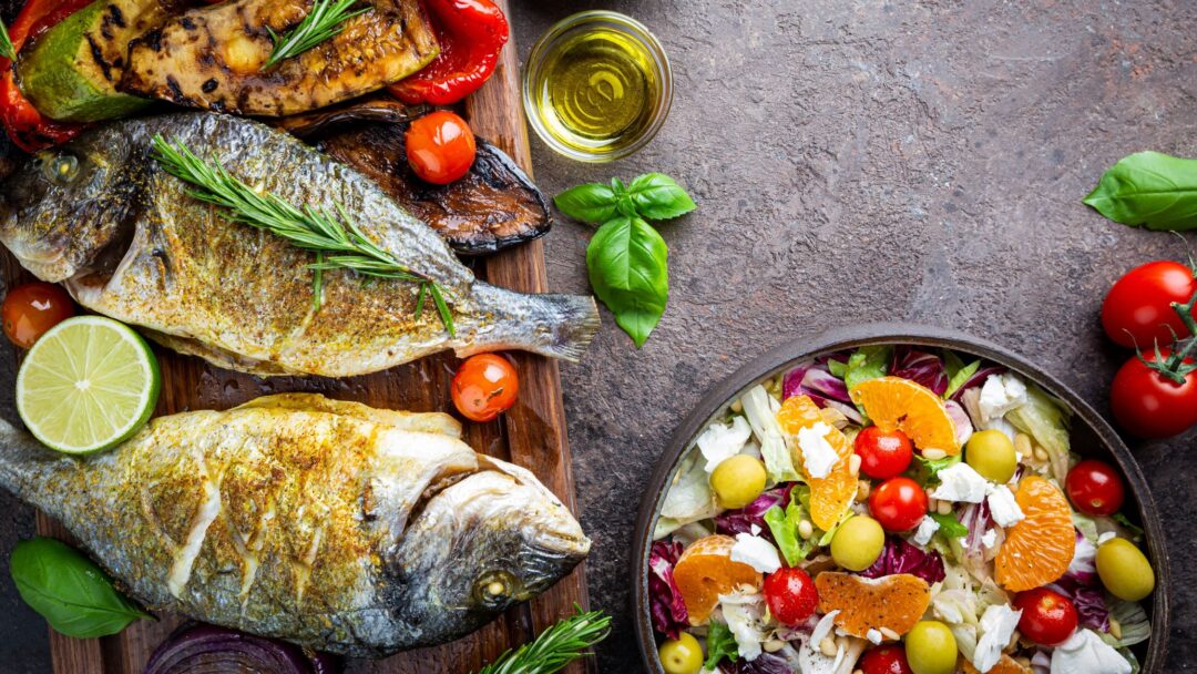 Gebratener Fisch auf einer Platte, daneben eine Schüssel mit Salat.