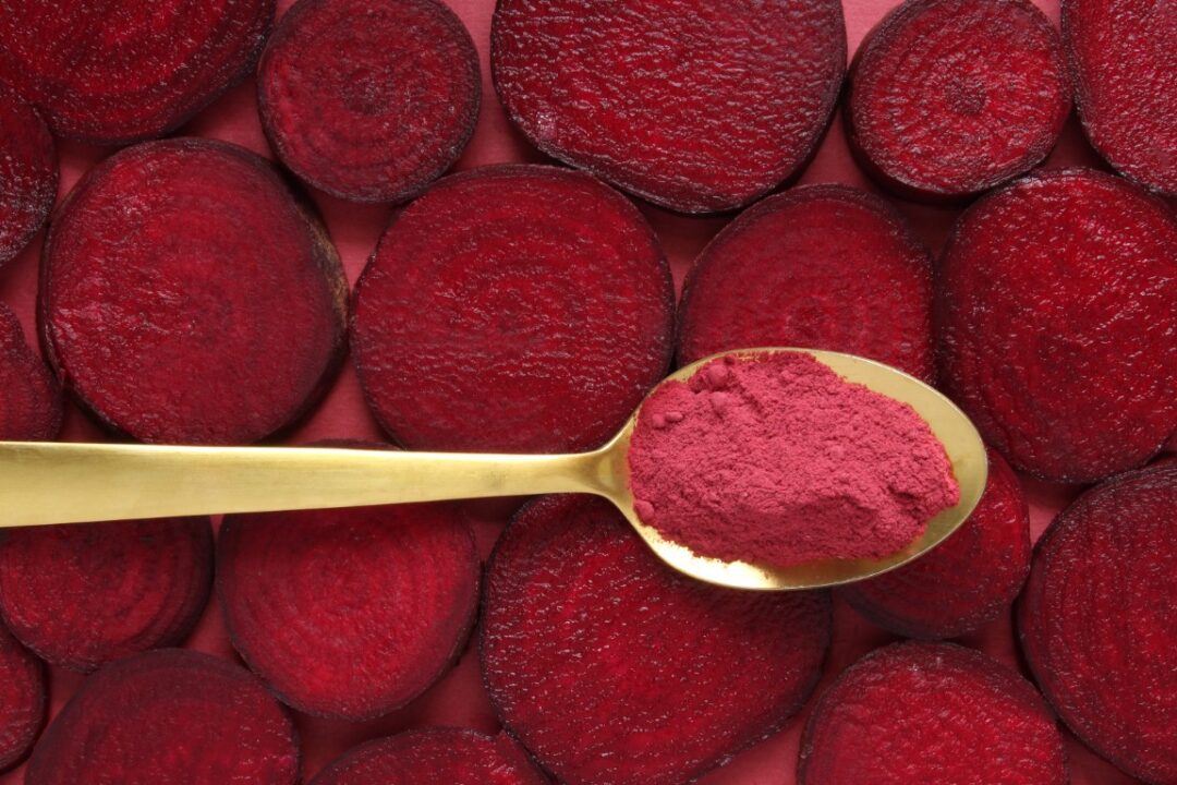 Augeschnittene Rote Bete und ein Löffel mit rotem Pulver (Betain)