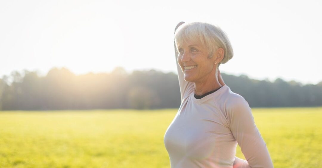 Ältere Frau beim Dehnen in der Natur als Beispiel für Bewegung zur Unterstützung gesunder Blutzucker- und Cholesterinwerte.